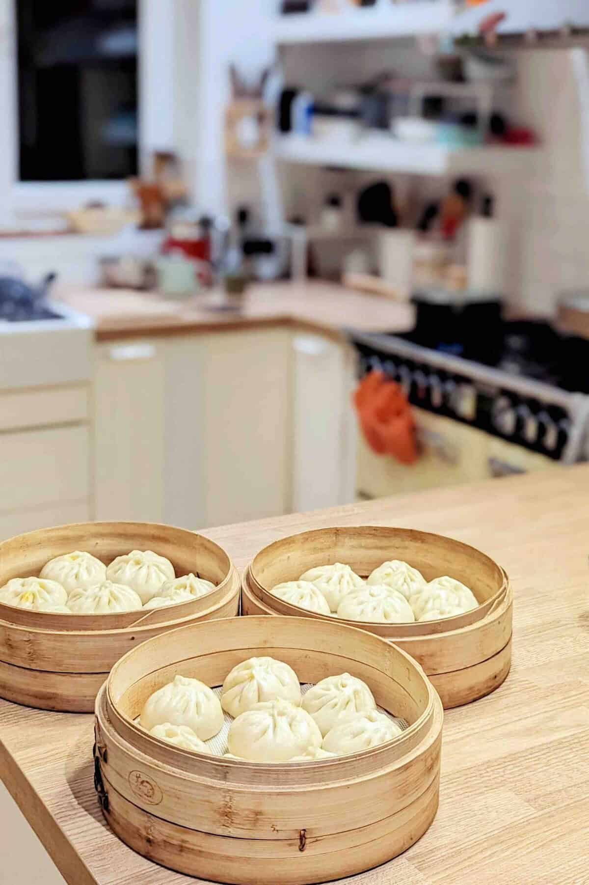 three layers of bamboo steamer baskets with bao buns in them.