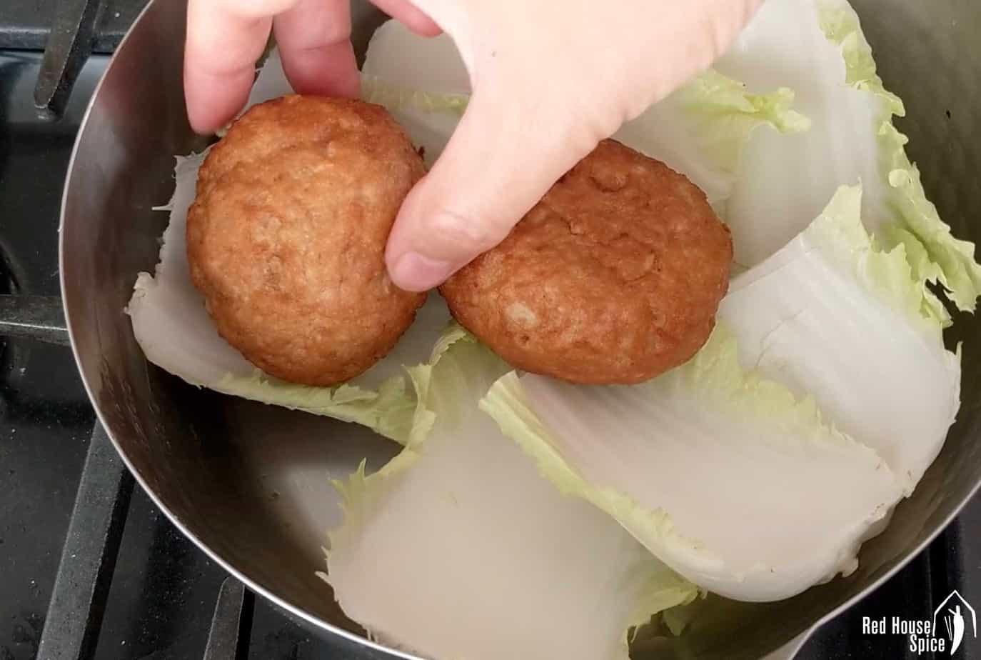 Putting meatballs into a pot over cabbage leaves